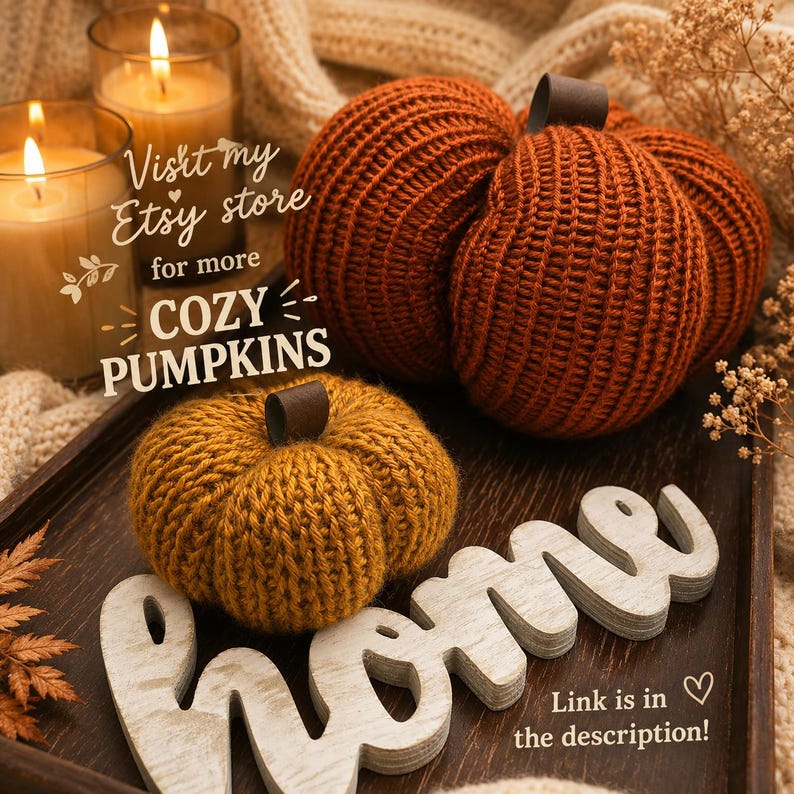 May include: Two knitted pumpkins in burnt orange and mustard yellow with dark brown stems, placed on a dark wooden tray next to a white wooden sign that reads home. Two lit candles in glass jars are visible in the background.