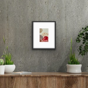 Puede incluir: Impresión artística enmarcada con una composición abstracta de formas orgánicas. La obra de arte presenta tonos rojos, marrones y beige sobre un fondo blanco. La impresión está encerrada en un marco negro, creando una estética moderna.