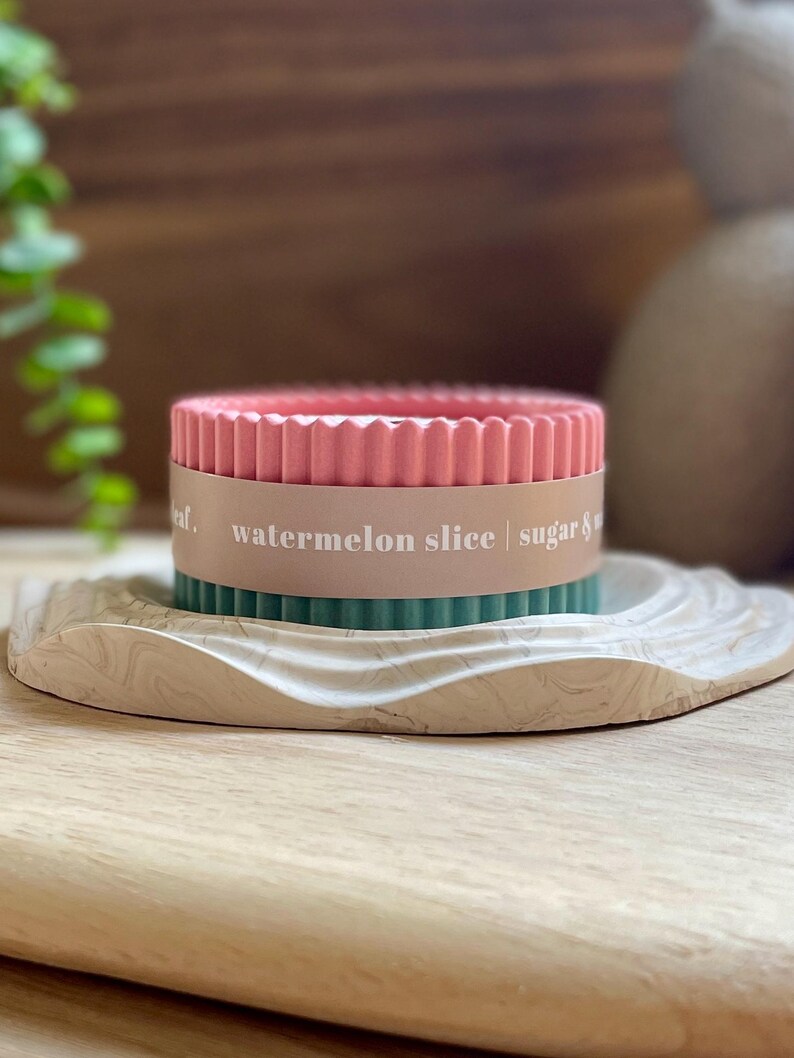 Puede incluir: Una vela rosa y verde con el texto "watermelon slice | sugar &" en una bandeja decorativa marmolada. La vela tiene un dise&ntilde;o acanalado y est&aacute; rodeada por una banda marr&oacute;n claro.