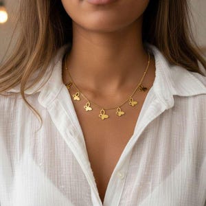 May include: A gold-colored butterfly pendant necklace. The necklace features multiple butterfly charms suspended from a delicate chain. The person in the image is wearing a white button-down shirt.