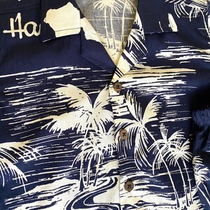 May include: A navy blue Hawaiian shirt with a white palm tree and river design. The shirt has a button-up front and a collar. The text "Ha" is visible on the left side of the shirt.