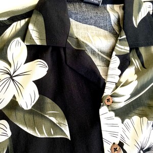 May include: Black and green Hawaiian shirt with white floral print. The shirt has a button-up collar and a care label that reads "Machine Wash Cold Water Like Colors Gentle Cycle Do Not Bleach Tumble Dry Low Warm Iron".