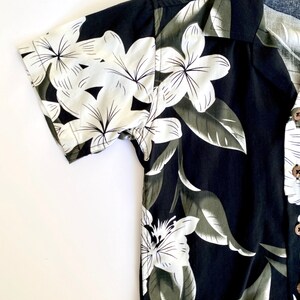 May include: A black short-sleeved button-up shirt with a white floral print. The shirt has a collar and a button-up front.