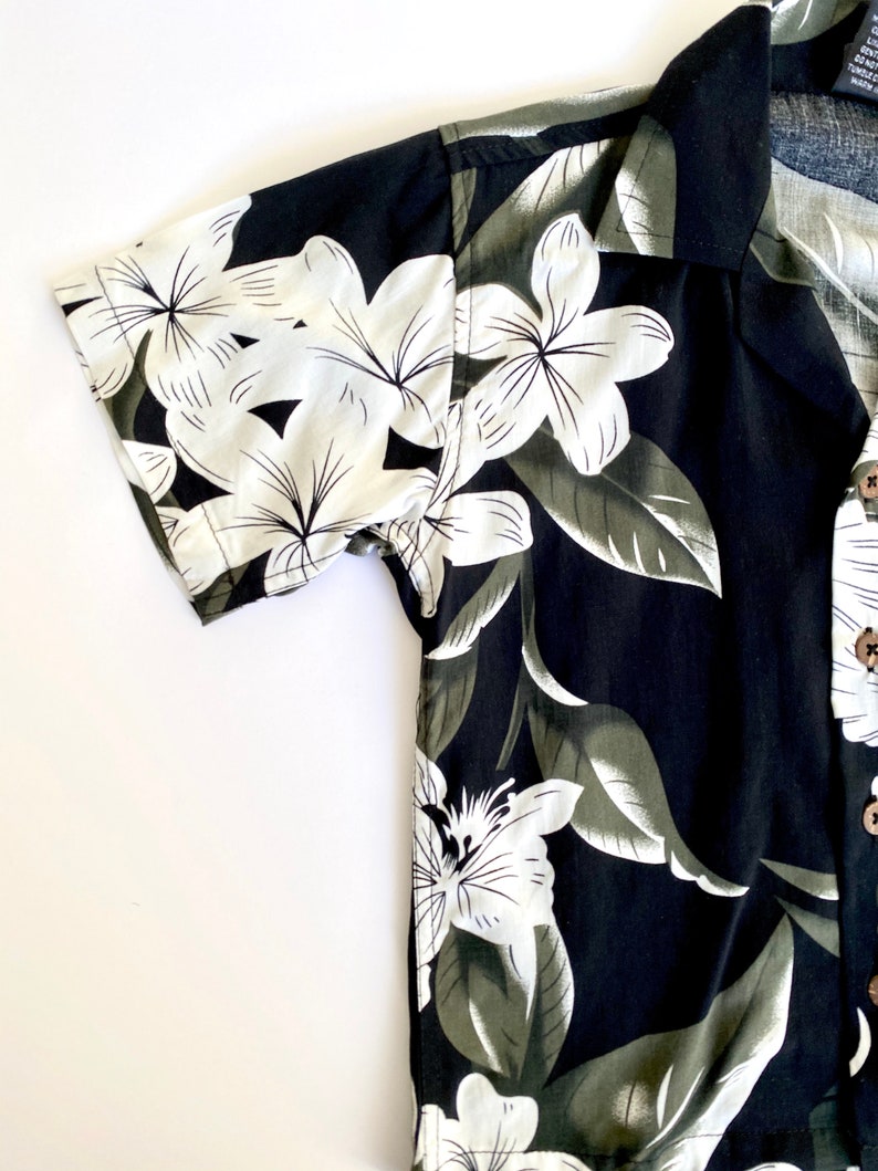 May include: A black short-sleeved button-up shirt with a white floral print. The shirt has a collar and a button-up front.