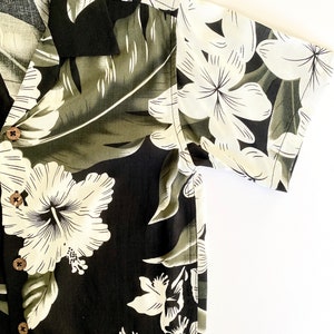 May include: A black and white floral print short-sleeved shirt with a button-up front. The shirt has a tropical theme with large white hibiscus flowers and green leaves.