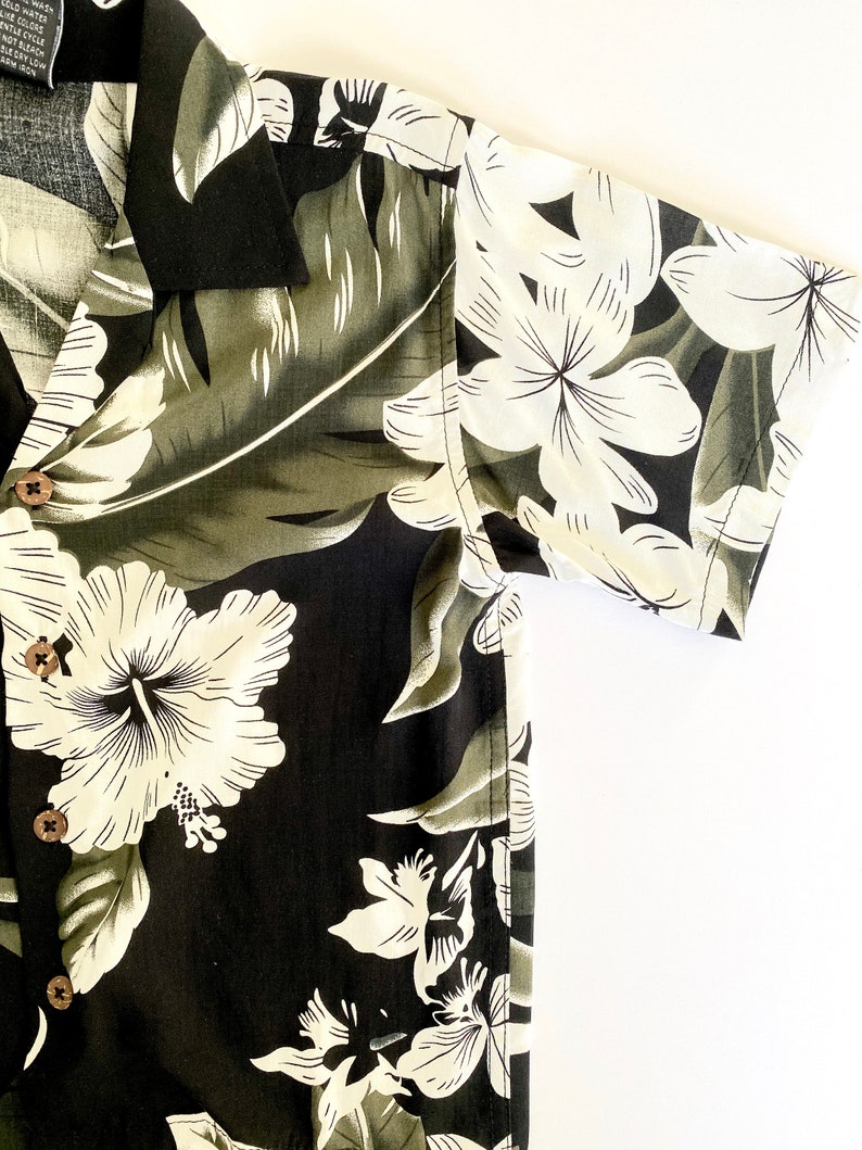 May include: A black and white floral print short-sleeved shirt with a button-up front. The shirt has a tropical theme with large white hibiscus flowers and green leaves.