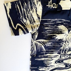 May include: A black and white short-sleeved button-up shirt with a palm tree and ocean scene. The shirt has the word "Hawaii" printed on the collar.