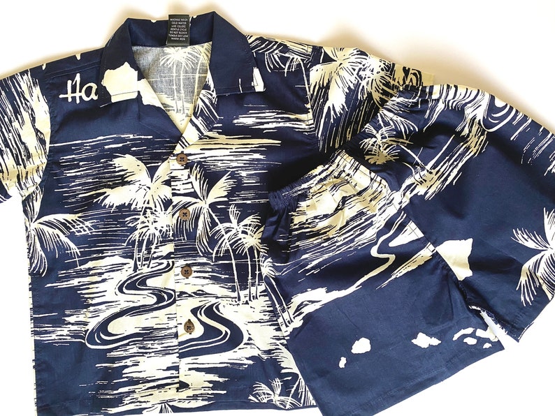 May include: A navy blue and white Hawaiian shirt and matching shorts set with a palm tree and river design. The shirt has a button-up front and short sleeves. The text "Ha" is embroidered on the left side of the shirt.