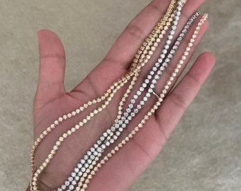 Op de afbeelding: Drie gouden kettingen met diamant accenten. De kettingen zijn op elkaar gelegd en worden in een hand gehouden. De kettingen zijn in verschillende goudkleuren: geel, wit en rosé.