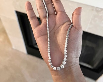 May include: A silver chain necklace with round, clear stones. The necklace is on a person's hand.
