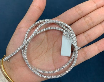 Op de afbeelding: Een zilveren tennisketting met kleine, ronde diamanten. De ketting is opgerold en wordt in een hand gehouden.
