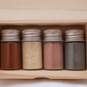 May include: A wooden box containing four small glass jars with different coloured powders. The jars have silver lids.