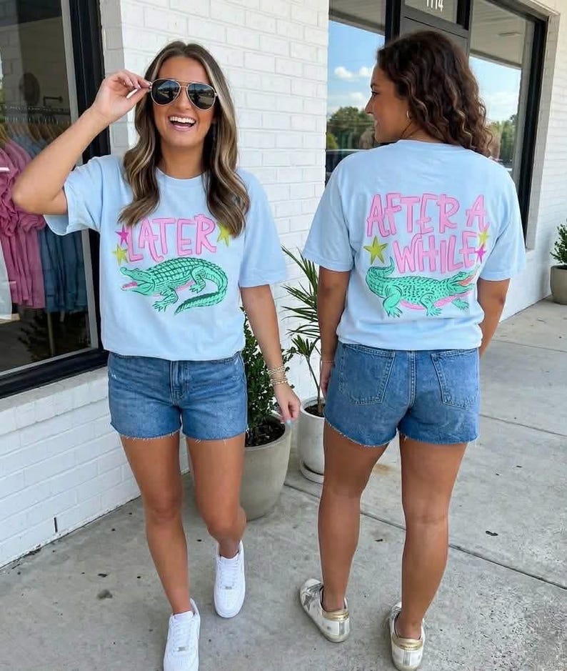 May include: Two people wearing light blue t-shirts and denim shorts. The front of the t-shirt has the word "LATER" above a green alligator graphic. The back of the t-shirt has the words "AFTER A WHILE" above the same alligator graphic.