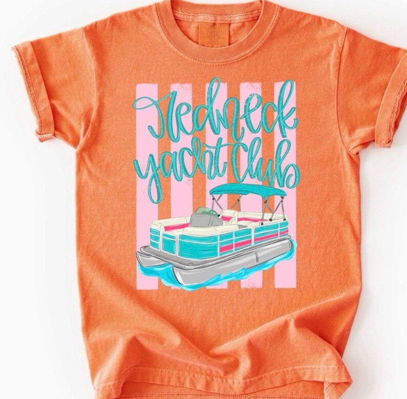 Pu&ograve; includere: T-shirt arancione con grafica di una barca pontone e la scritta "Redneck Yacht Club" in corsivo turchese. Il design della barca include dettagli turchesi, rosa e argento. Lo sfondo presenta strisce verticali rosa.