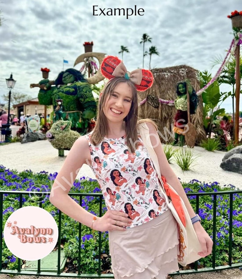 May include: A woman wearing a white tank top with a repeating graphic print. She is also wearing a headband with large red and brown ears and a large bow. The image has the word "Example" at the top.