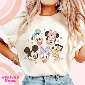 Puede incluir: Sudadera color crema con un gr&aacute;fico colorido de los personajes de Disney Mickey Mouse, Minnie Mouse, Donald Duck, Daisy Duck y Pluto, con acentos de estrellas. El texto "Avalynn Bows" est&aacute; en la parte inferior.