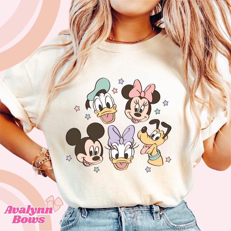 Puede incluir: Sudadera color crema con un gr&aacute;fico colorido de los personajes de Disney Mickey Mouse, Minnie Mouse, Donald Duck, Daisy Duck y Pluto, con acentos de estrellas. El texto "Avalynn Bows" est&aacute; en la parte inferior.