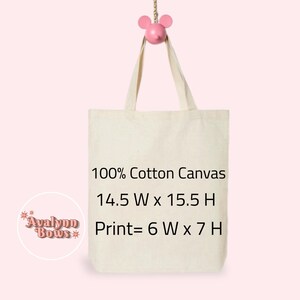 May include: Cream-coloured tote bag made of 100% cotton canvas. The bag is hanging from a pink mouse-shaped hook. Text on the bag reads: 14.5" W x 15.5" H, Print= 6" W x 7" H. The bag has a simple design, perfect for carrying items.
