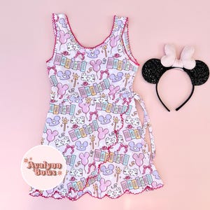 Puede incluir: Un vestido sin mangas con fondo morado claro que presenta un patr&oacute;n repetitivo de globos con forma de rat&oacute;n rosas y morados, varitas, lazos y la palabra magical, junto a una diadema negra brillante con un lazo rosa claro.