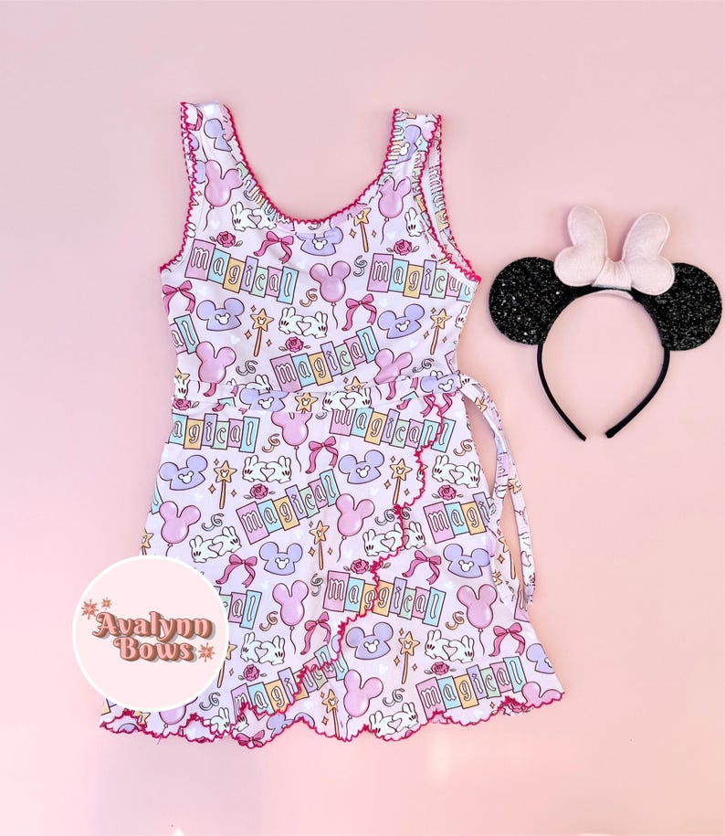 Puede incluir: Un vestido sin mangas con fondo morado claro que presenta un patr&oacute;n repetitivo de globos con forma de rat&oacute;n rosas y morados, varitas, lazos y la palabra magical, junto a una diadema negra brillante con un lazo rosa claro.