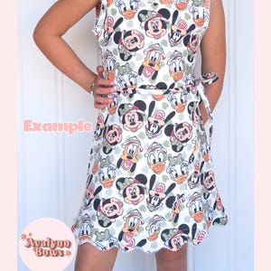 Puede incluir: Un vestido sin mangas con un estampado integral de personajes de Disney, incluyendo a Mickey Mouse, Minnie Mouse, el Pato Donald y Daisy con sombreros de safari. El vestido tiene cuello redondo, un lazo en la cintura y un borde festoneado blanco.