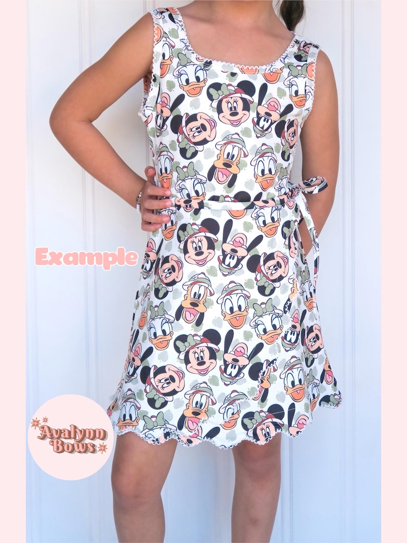 Puede incluir: Un vestido sin mangas con un estampado integral de personajes de Disney, incluyendo a Mickey Mouse, Minnie Mouse, el Pato Donald y Daisy con sombreros de safari. El vestido tiene cuello redondo, un lazo en la cintura y un borde festoneado blanco.