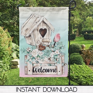 Puede incluir: Una bandera de jardín de bienvenida con una casita de pájaros, flores y un pájaro. La casita de pájaros está hecha de madera y tiene una abertura en forma de corazón. Las flores son blancas y rosas. El pájaro es rojo con el pecho blanco. La bandera está impresa sobre un fondo blanco con un degradado de azul claro y rosa.
