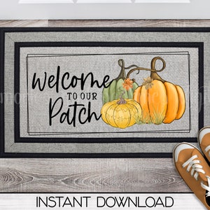 May include: A welcome mat with a gray background and black border. The text "Welcome to our Patch" is written in black. There are three pumpkins, one green, one yellow, and one orange, with fall leaves and vines.