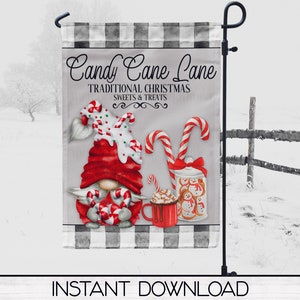 Peut inclure: Un drapeau de jardin de Noël avec un gnome. Le drapeau affiche le texte "Candy Cane Lane" et présente un gnome avec un chapeau rouge, des cannes en bonbon, un pot de biscuits et une tasse de chocolat chaud. Fond enneigé.
