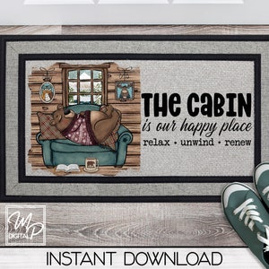 Puede incluir: Una alfombra de bienvenida de color gris con un borde negro. La alfombra presenta una ilustración de dibujos animados de un oso con un suéter durmiendo en un sillón azul. El texto "THE CABIN is our happy place relax unwind renew" está impreso en negro en la alfombra.