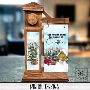 May include: A wooden sign featuring a Christmas scene with the text "All roads lead to home at Christmas". The sign is decorated with a red truck, a cabin, and a Christmas tree.