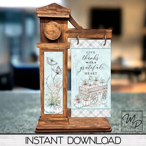 Könnte beinhalten: Ein Holzschild mit blau-weißem kariertem Hintergrund. Das Schild zeigt eine handgezeichnete Illustration eines Wagens voller Kürbisse und den Text "Give thanks with a grateful heart".