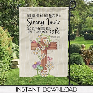 May include: A beige garden flag with a brown wooden cross surrounded by white flowers and a ladybug. The text on the flag reads "The name of the Lord is a Strong Tower. The Righteous run into it and are safe. Proverbs 18:10"