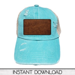 以下が含まれることがあります： ターコイズブルーとベージュのダメージ加工が施されたトラッカーハット。茶色の革のパッチが付いています。メッシュバックとカーブしたつばが付いています。