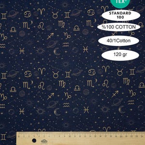 Op de afbeelding: Marineblauwe stof met een gouden hemels patroon met sterrenbeelden, planeten, sterren en manen. De stof heeft tekst die luidt "STANDARD 100", "%100 COTTON", "40/1 Cotton" en "120 gr". Onderaan staat een houten liniaal.