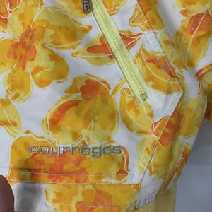 May include: White jacket with a vibrant floral pattern in yellow and orange. Features a yellow zipper and the brand name "courr&egrave;ges" in silver lettering. The jacket has a soft, yellow lining.