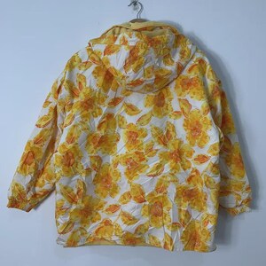 May include: A hooded jacket with a floral pattern in shades of yellow and orange on a white background. The jacket has long sleeves and a drawstring hood. The jacket is hanging on a metal hanger.
