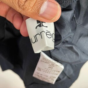 May include: Close-up of a white label with the brand name "courr&egrave;ges" printed in black. The label is attached to a dark navy blue garment. The garment's lining is visible.