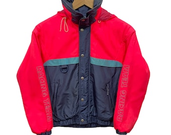 May include: A red and navy blue hooded jacket with the words "Racing Team" printed on the sleeves. The jacket has a zipper closure and a drawstring hood.