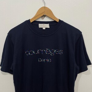 Op de afbeelding: Een marineblauw T-shirt met een kleurrijk "Courr&egrave;ges Paris" logo geborduurd op de voorkant.