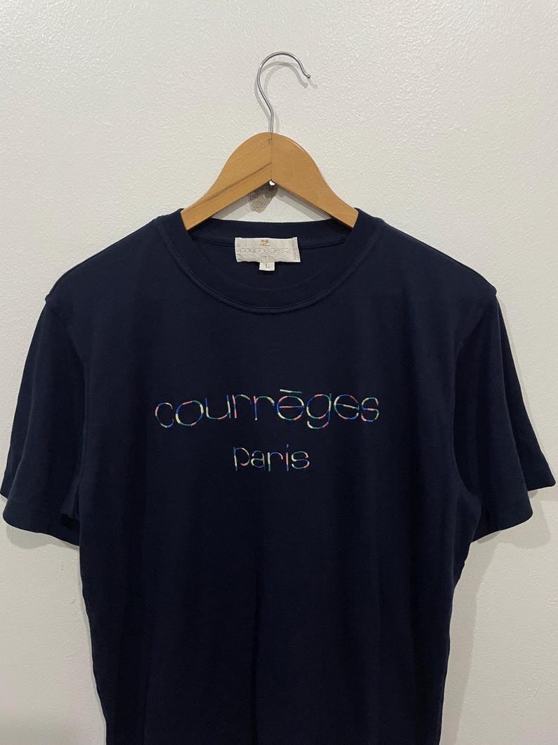 Op de afbeelding: Een marineblauw T-shirt met een kleurrijk "Courr&egrave;ges Paris" logo geborduurd op de voorkant.