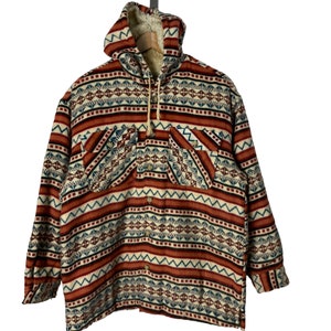 Pode incluir: Uma camisa de flanela com capuz com um padrão geométrico em tons de vermelho, azul, branco e preto. A camisa tem um fecho de botões na frente e um capuz com cordão.