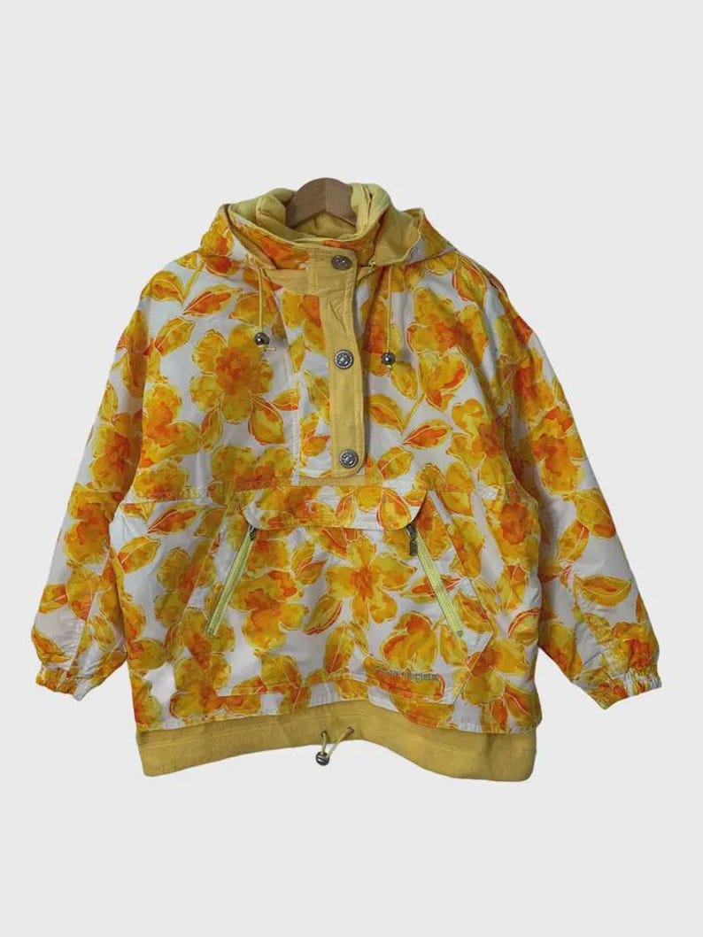 May include: A vintage anorak jacket with a floral pattern in yellow and orange on a white background. The jacket has a hood, a button-up front, and two front pockets with yellow zippers. The cuffs and hem are yellow.