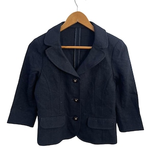 May include: A black blazer with three buttons and two front pockets, hanging on a wooden hanger. The blazer has three-quarter sleeves and a classic lapel design. The garment is made of a textured fabric.