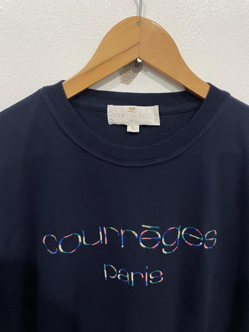 Op de afbeelding: Een marineblauw t-shirt met een meerkleurig geborduurd "Courr&egrave;ges Paris" logo.