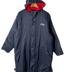 Pu&ograve; includere: Una giacca blu navy con cappuccio, fodera rossa e logo FILA bianco sul davanti. La giacca ha una chiusura con bottoni e due tasche.