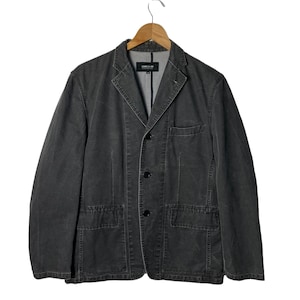 May include: A dark grey blazer with a button closure and multiple pockets. The blazer has a label that reads "Comme des Garçons" on the inside.