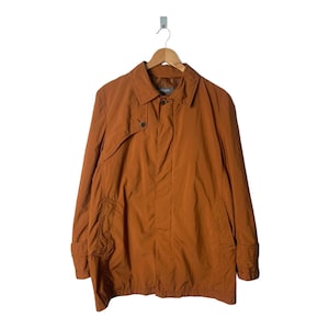 Puede incluir: Una chaqueta larga de manga larga de color marrón con cierre de botones y un bolsillo de solapa en el lado izquierdo.