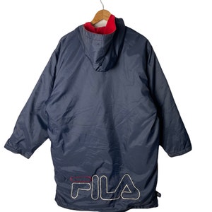 Pu&ograve; includere: Una giacca blu navy con cappuccio, fodera in pile rosso e logo FILA bianco sul retro.