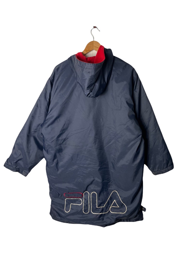 Pu&ograve; includere: Una giacca blu navy con cappuccio, fodera in pile rosso e logo FILA bianco sul retro.